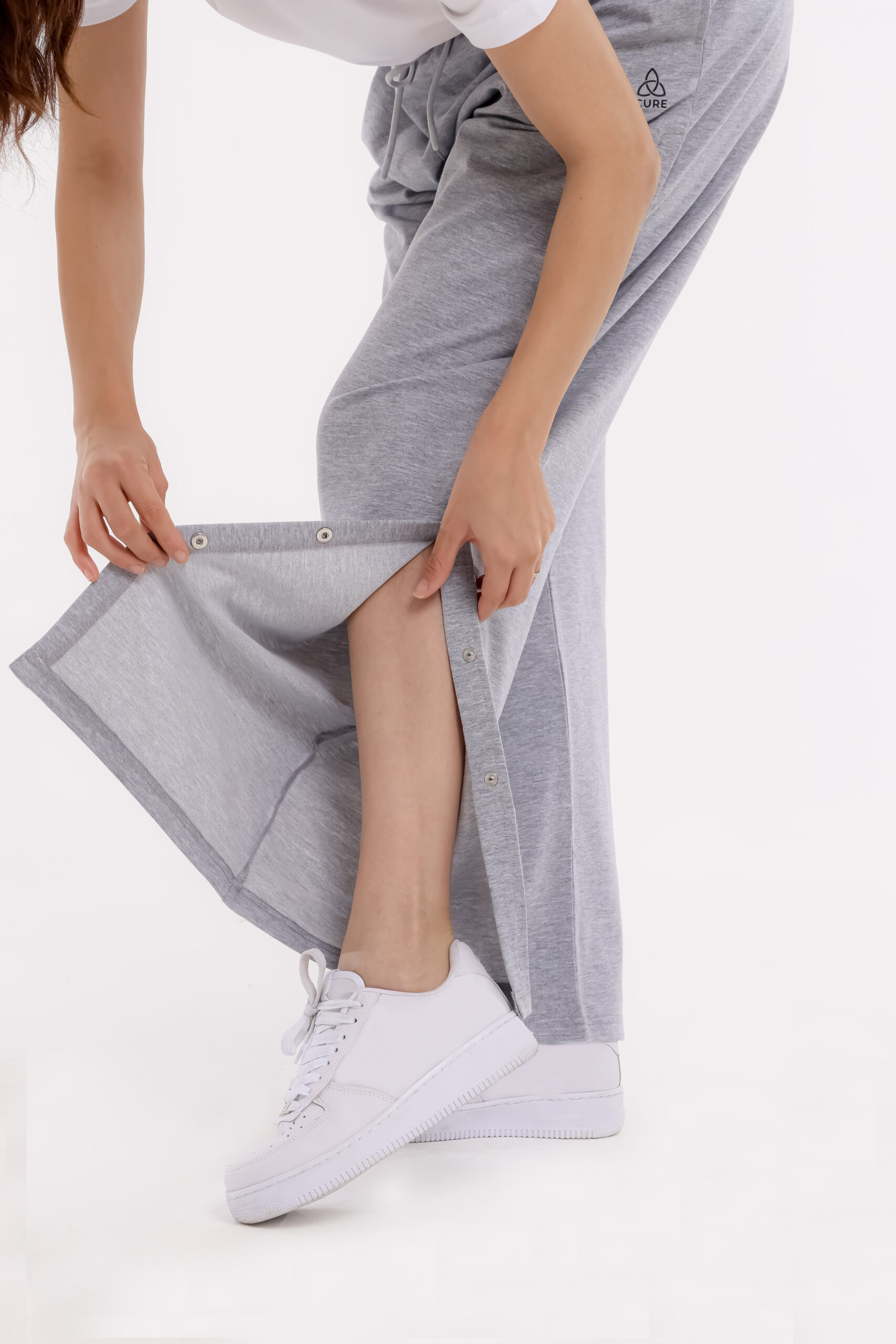 Frau öffnet seitliche Druckknöpfe an grauer orthopädischer Behandlungshose – geeignet für Pflege und Therapie