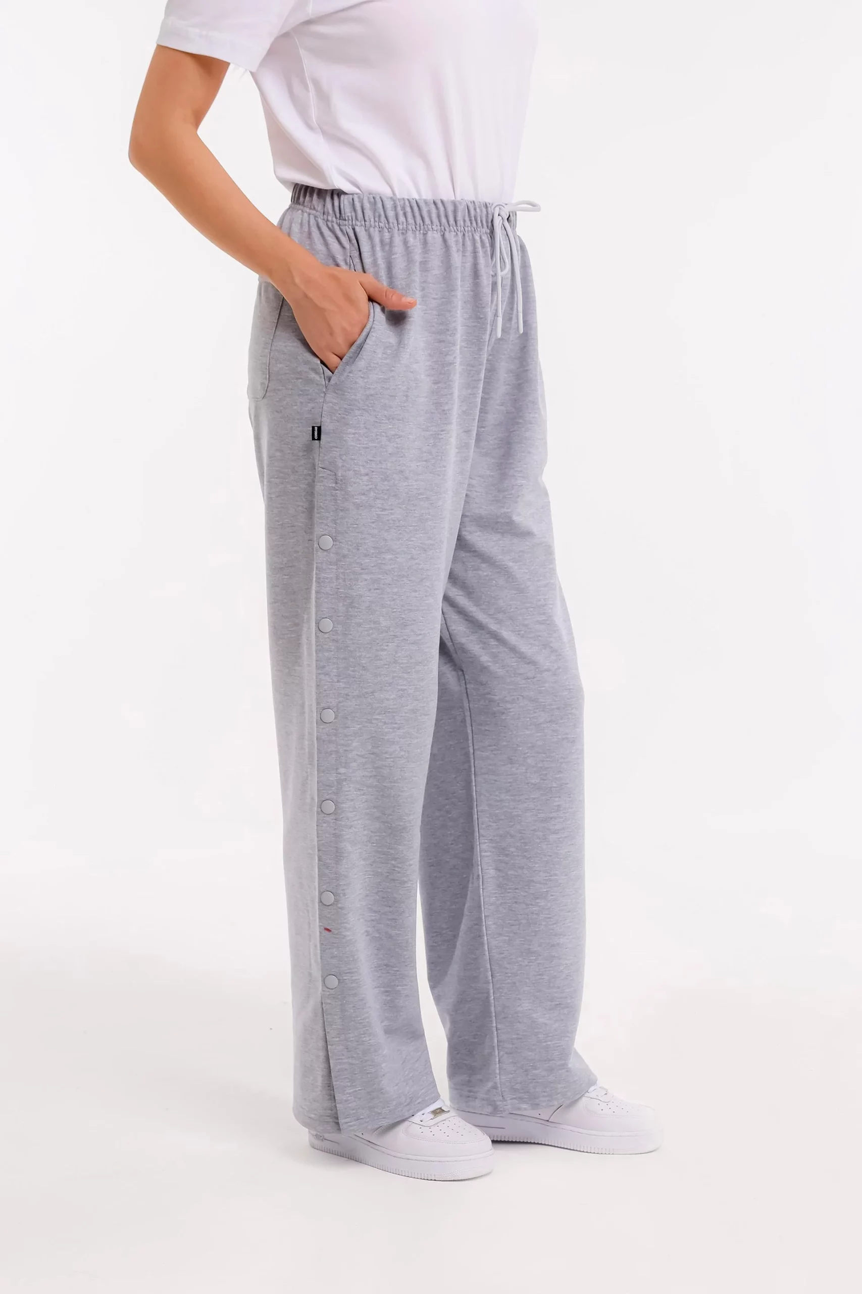 Seitliche Detailansicht der grauen orthopädischen Behandlungshose mit sichtbarer Druckknopfleiste und Hand in Hosentasche