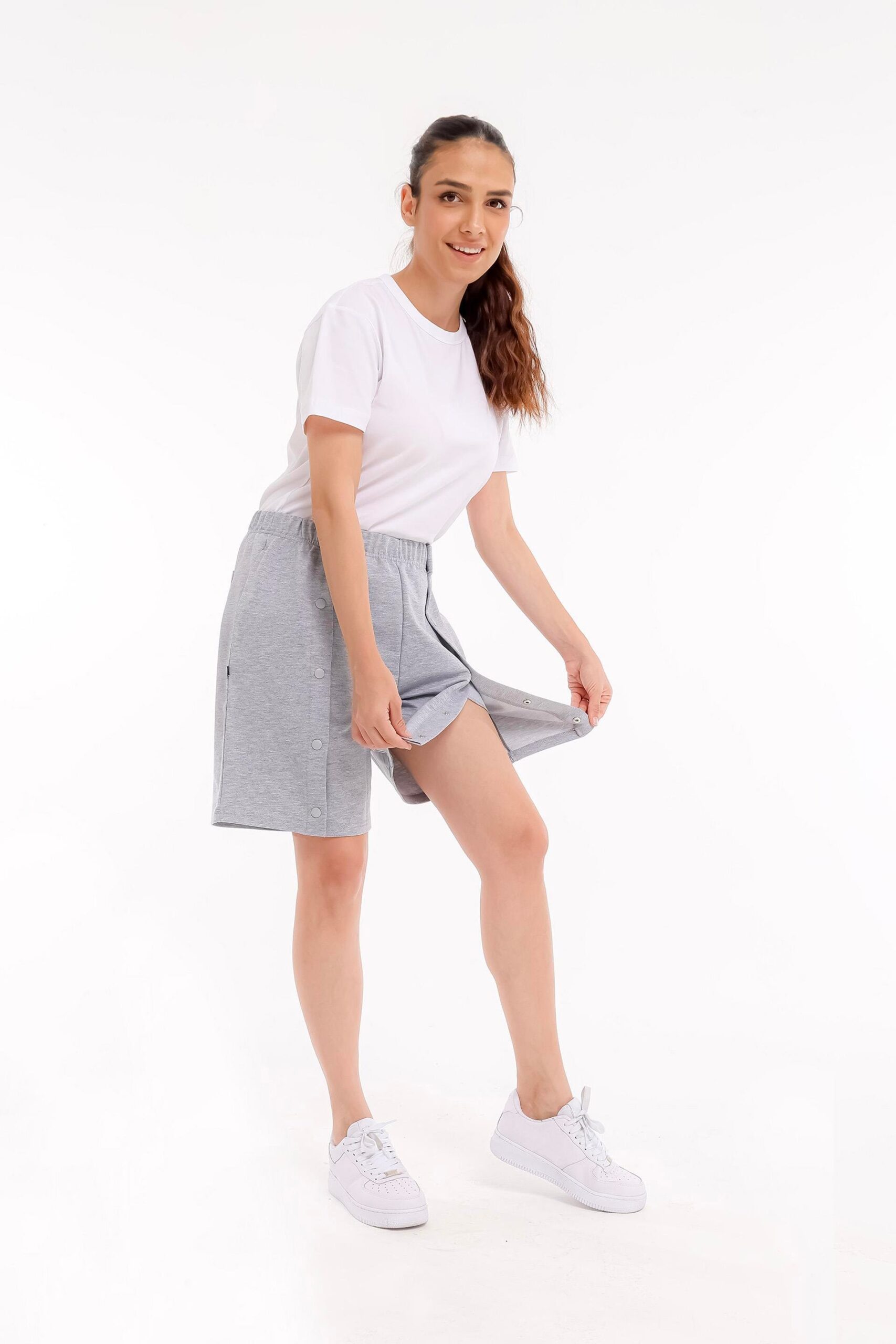 Demonstration der seitlichen Öffnung der grauen stationären Shorts für Damen mit Druckknopfleiste